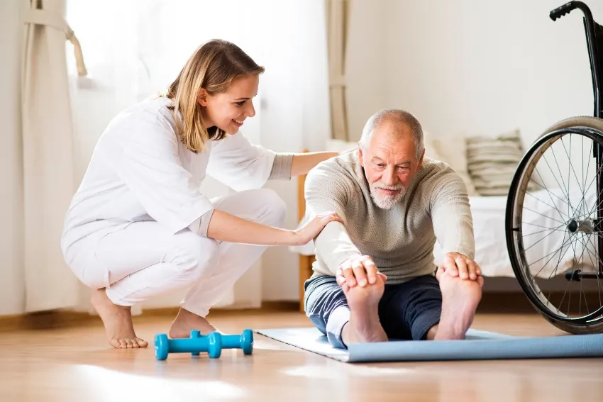 Physiotherapist helping an older man with a stretching exercise at home